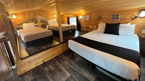 Un dormitorio tipo cabaña de madera con dos camas, una cama grande, una escalera de madera y un ventanal pequeño.