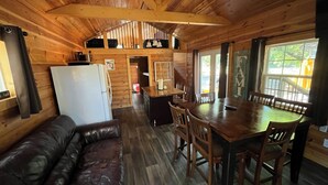 Interior de una cabaña de madera con comedor, cocina y sala de estar.