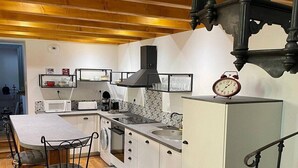 Een kleine keuken met een centraal eiland, witte kasten, een zwarte afzuigkap en een klok in vintage-stijl.
