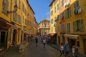 Eine Kopfsteinpflasterstraße säumen gelbe Gebäude, einige mit Markisen und Schildern, unter blauem Himmel.