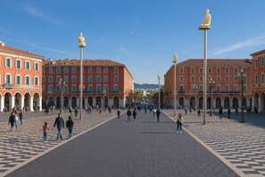 Ein weitläufiger öffentlicher Platz mit einer zentralen, offenen Fläche, umgeben von Gebäuden mit Rundbogenfenstern und einem Kachelboden.
