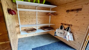 Puinen sisustus, jossa on valkoinen hyllykkö, jossa on koreja ja laukkuja, sekä seinälle kiinnitetty teline laukuille.