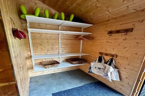 A wooden interior with a white shelf unit holding baskets and bags, and a wall-mounted rack with bags. - Spacious French Chalet Stay for 10 (Mont-Dore)