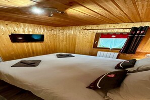 A wooden-paneled room with a bed, a flat-screen TV, a window with curtains, and a radiator. - Spacious French Chalet Stay for 10 (Mont-Dore)