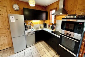 A compact kitchen with a refrigerator, dishwasher, stove, oven, and a sink. - Spacious French Chalet Stay for 10 (Mont-Dore)