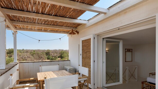 A covered outdoor seating area with a table and chairs, a refrigerator, and a sliding glass door leading to an interior space. - Apartment 'Tenuta Degli Asinelli - Casale' with Sea View, Wi-Fi and Air Conditioning (Alliste)