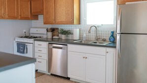 Una cocina con armarios de madera, un refrigerador de acero inoxidable, un lavavajillas y una ventana sobre el fregadero.