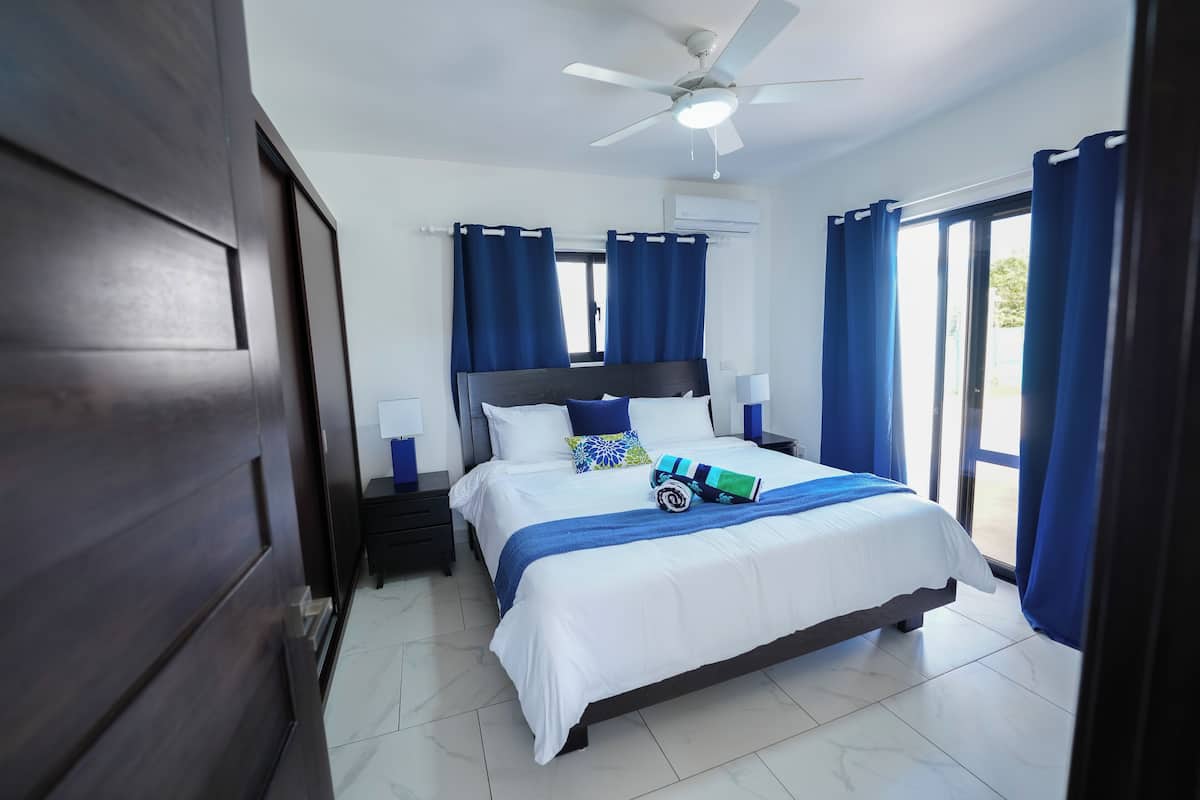 A bedroom with a bed, nightstands, a ceiling fan, and a window with curtains.