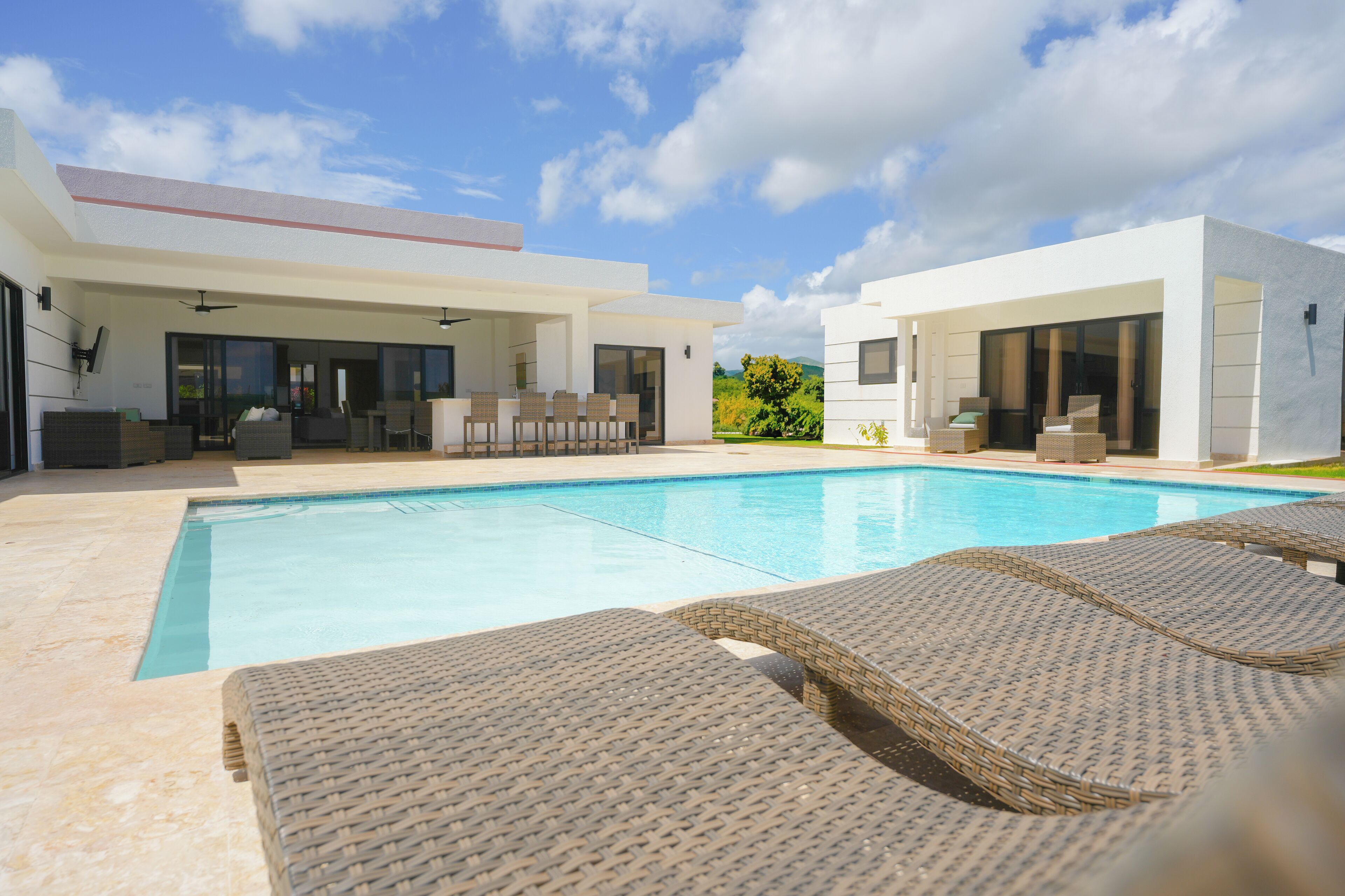 A modern outdoor pool area with lounge chairs, a covered seating area, and a clear blue sky.