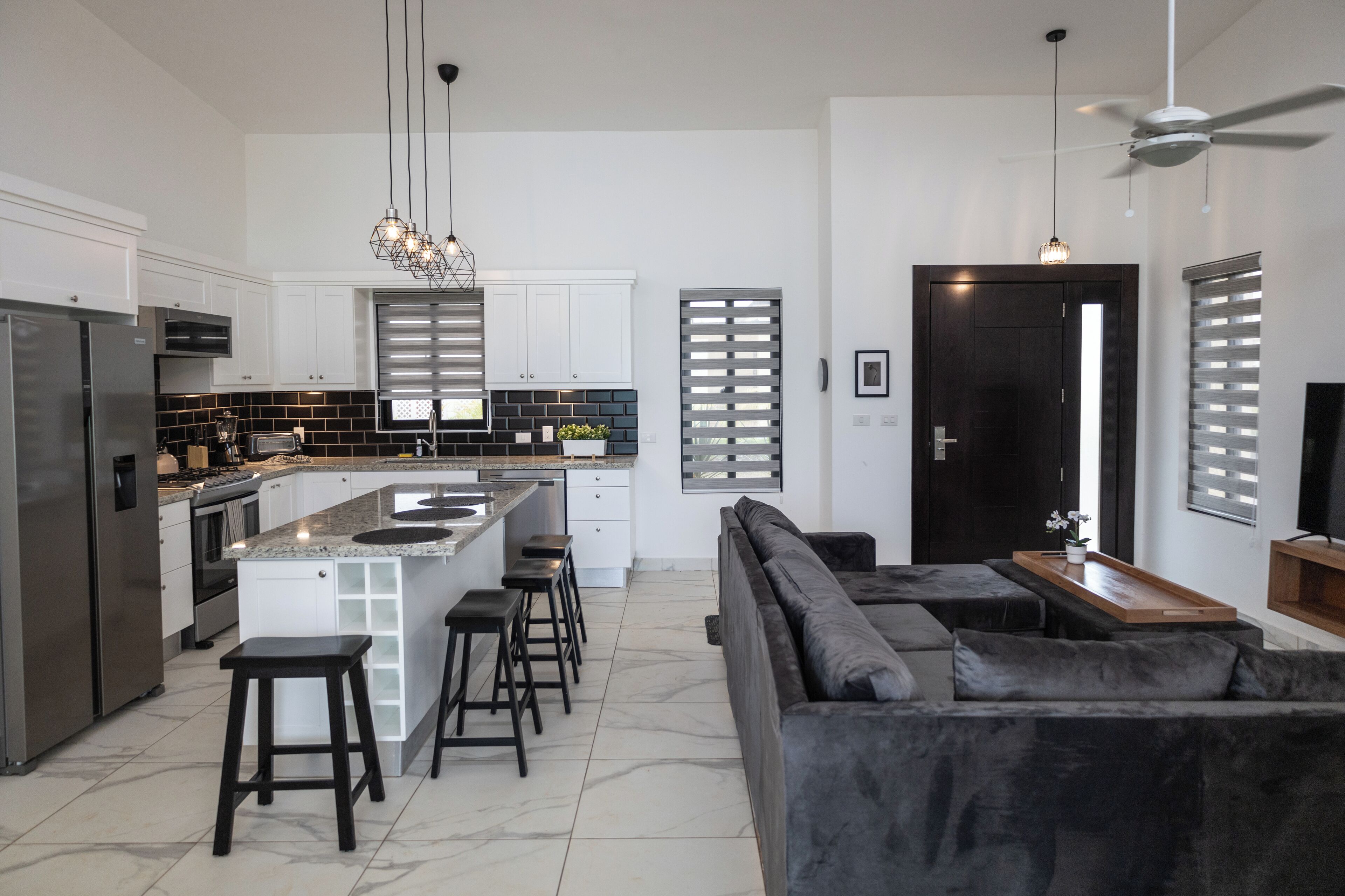 A modern kitchen with white cabinets, a black backsplash, and a central island with stools.