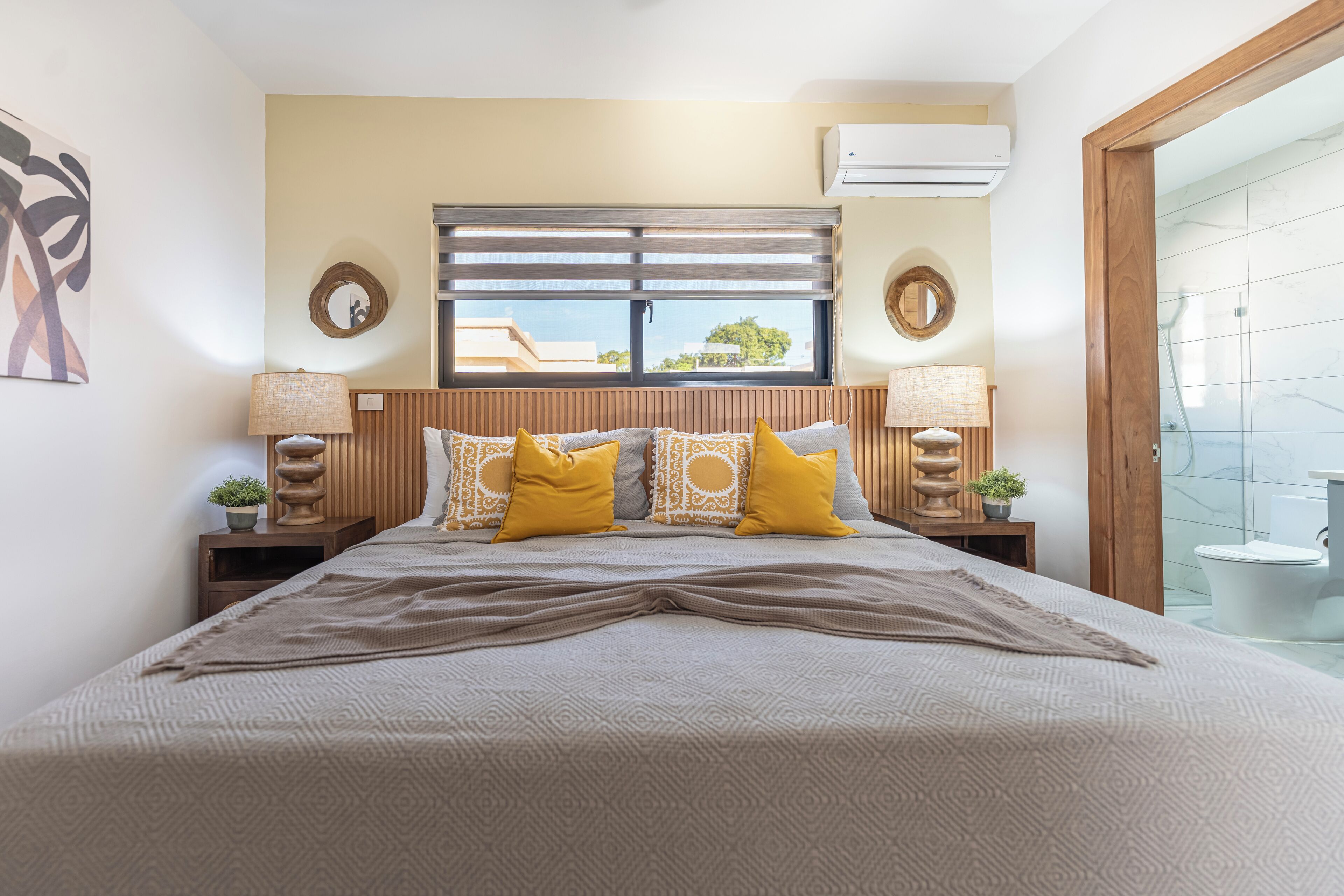 Un dormitorio con una cama grande, dos mesitas de noche con lámparas, un ventanal con persianas y vistas al exterior.