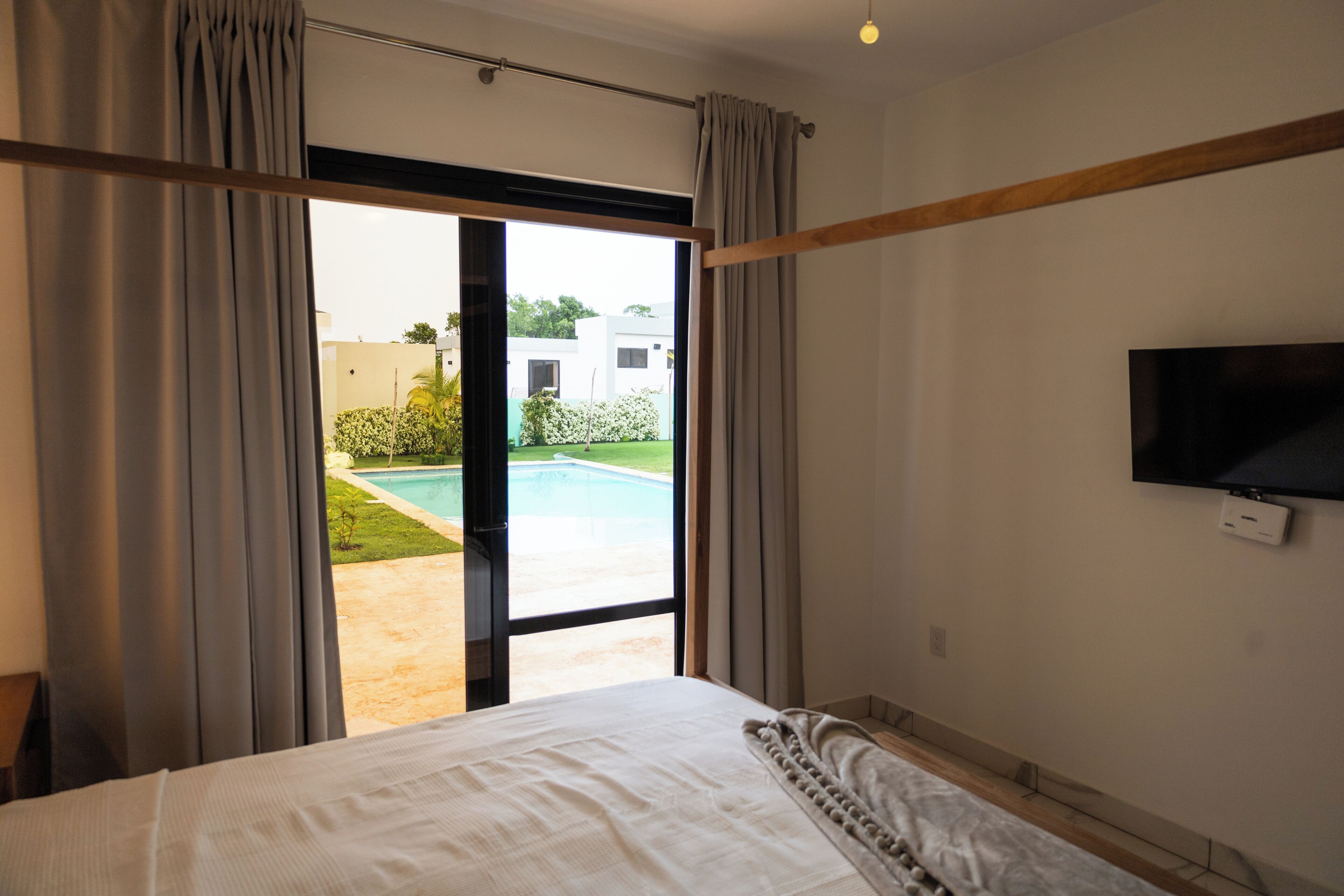 Une chambre dotée d’un grand lit, d’un téléviseur fixé au mur et d’une porte-fenêtre coulissante donnant sur une zone abritant une piscine.