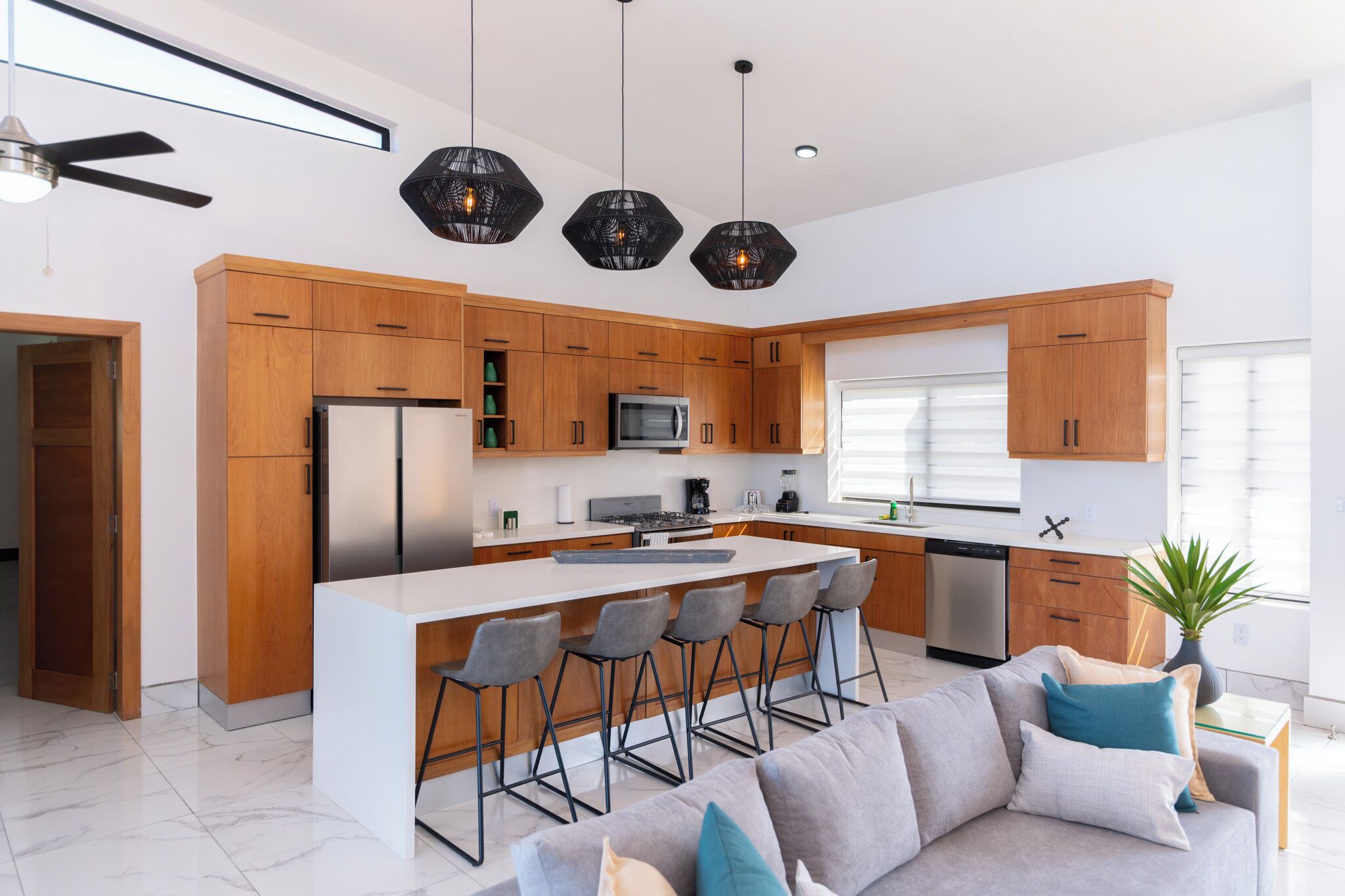 A modern kitchen with wooden cabinets, a central island with bar stools, a built-in microwave, and a large window.