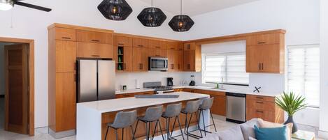 A modern kitchen with wooden cabinets, a central island with bar stools, a built-in microwave, and a large window.