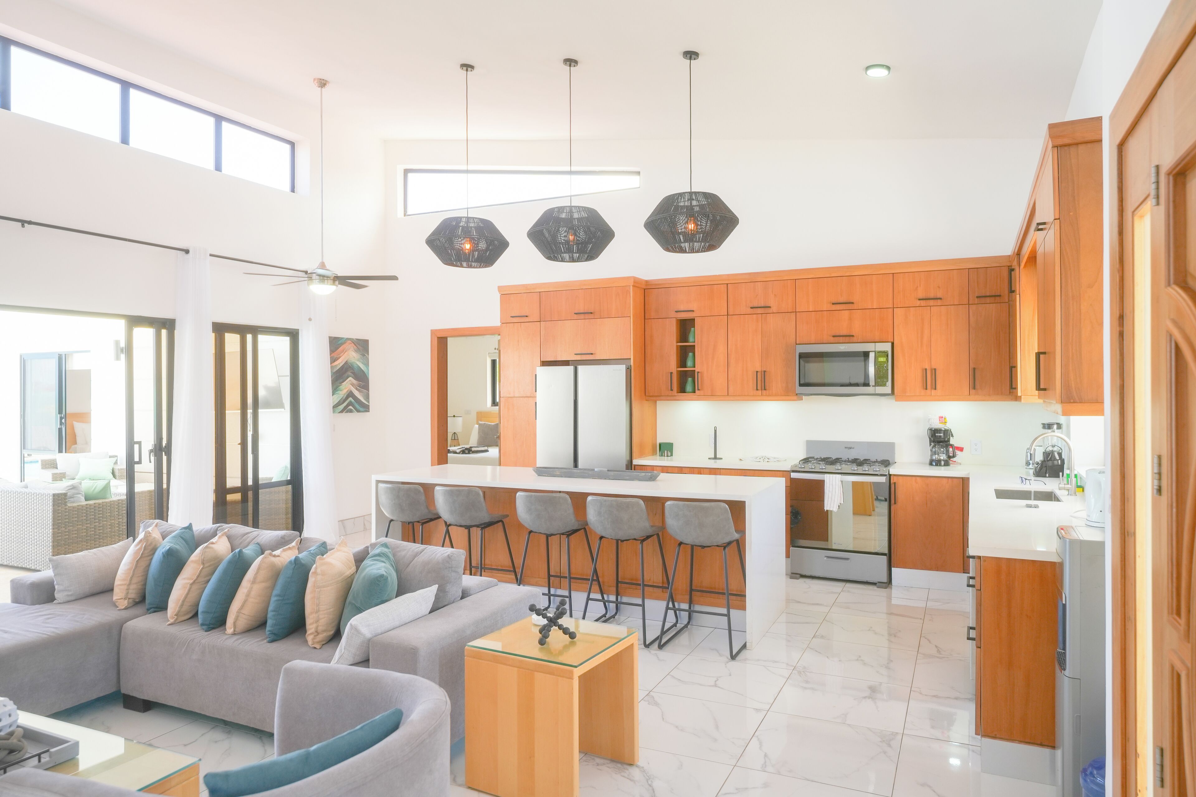 A modern kitchen with wooden cabinets, a central island with bar stools, a refrigerator, and a microwave.