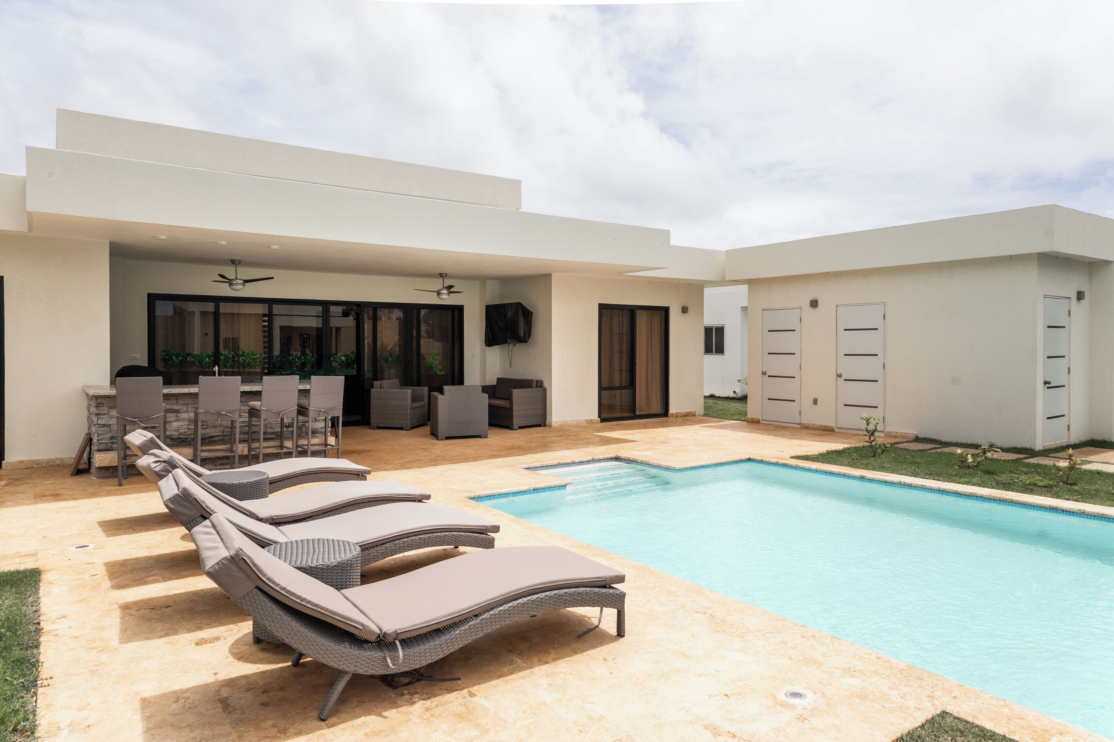 A modern outdoor pool area with lounge chairs, a barbecue setup, and a covered seating area.