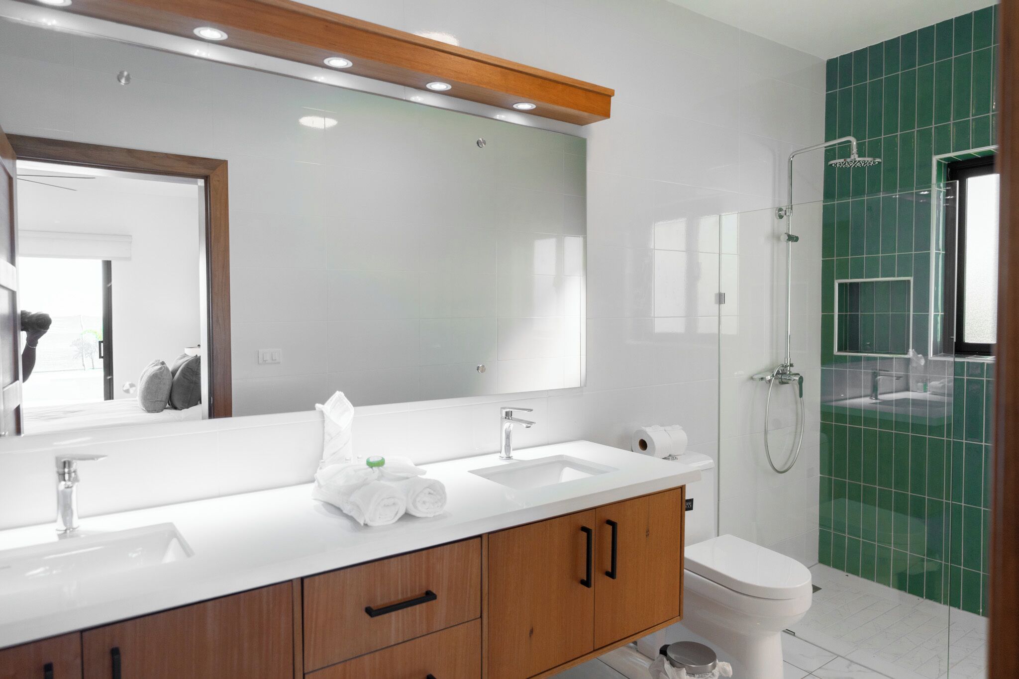 Un baño moderno con un espejo grande, dos lavamanos, un inodoro y una ducha.