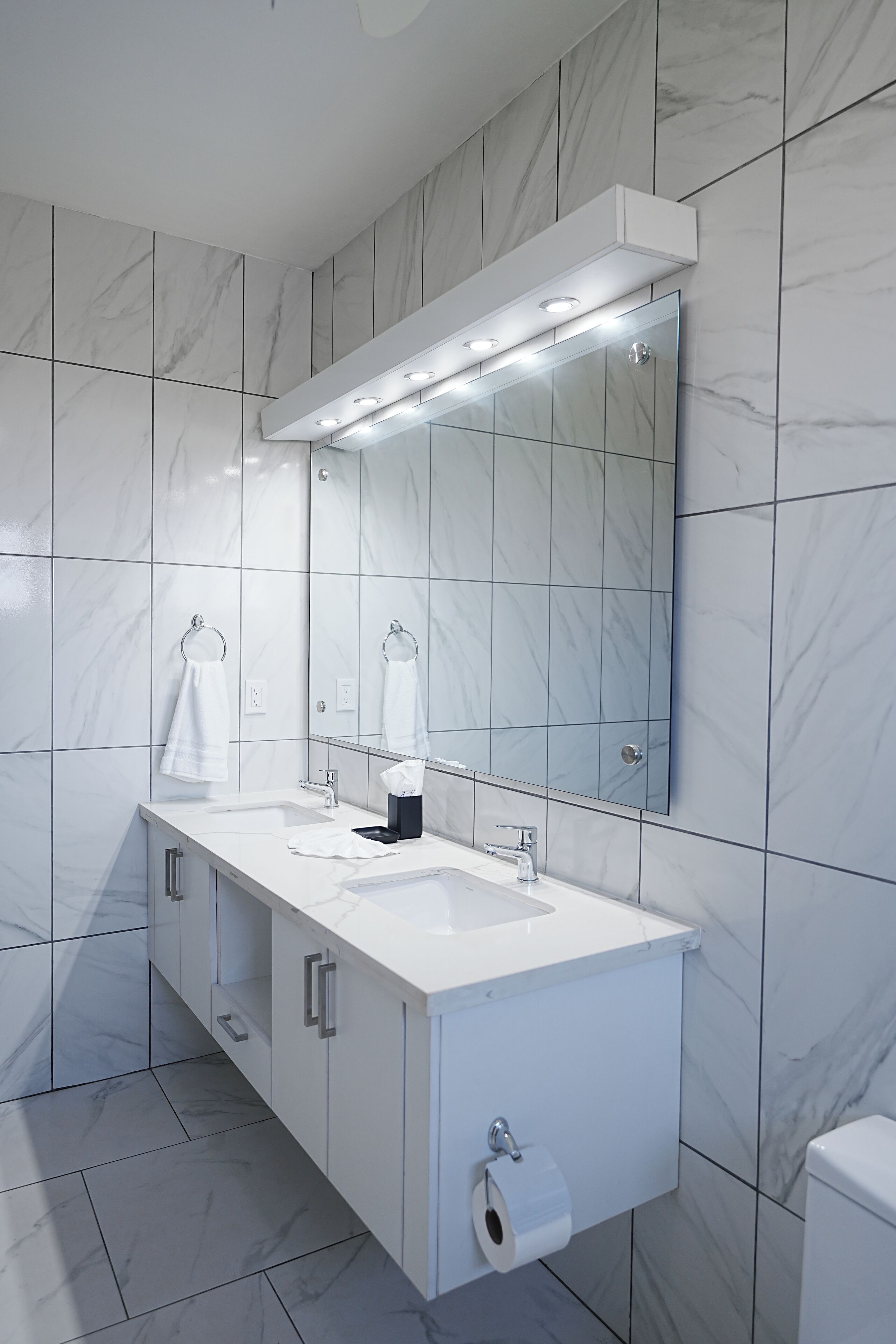 A modern bathroom with a white vanity, a large mirror, and a toilet.