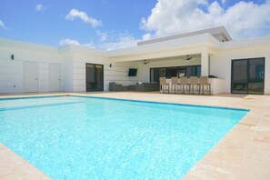 Ein modernes Haus mit Schwimmbad, einer überdachten Terrasse mit Sitzgelegenheit und großen Fenstern.
