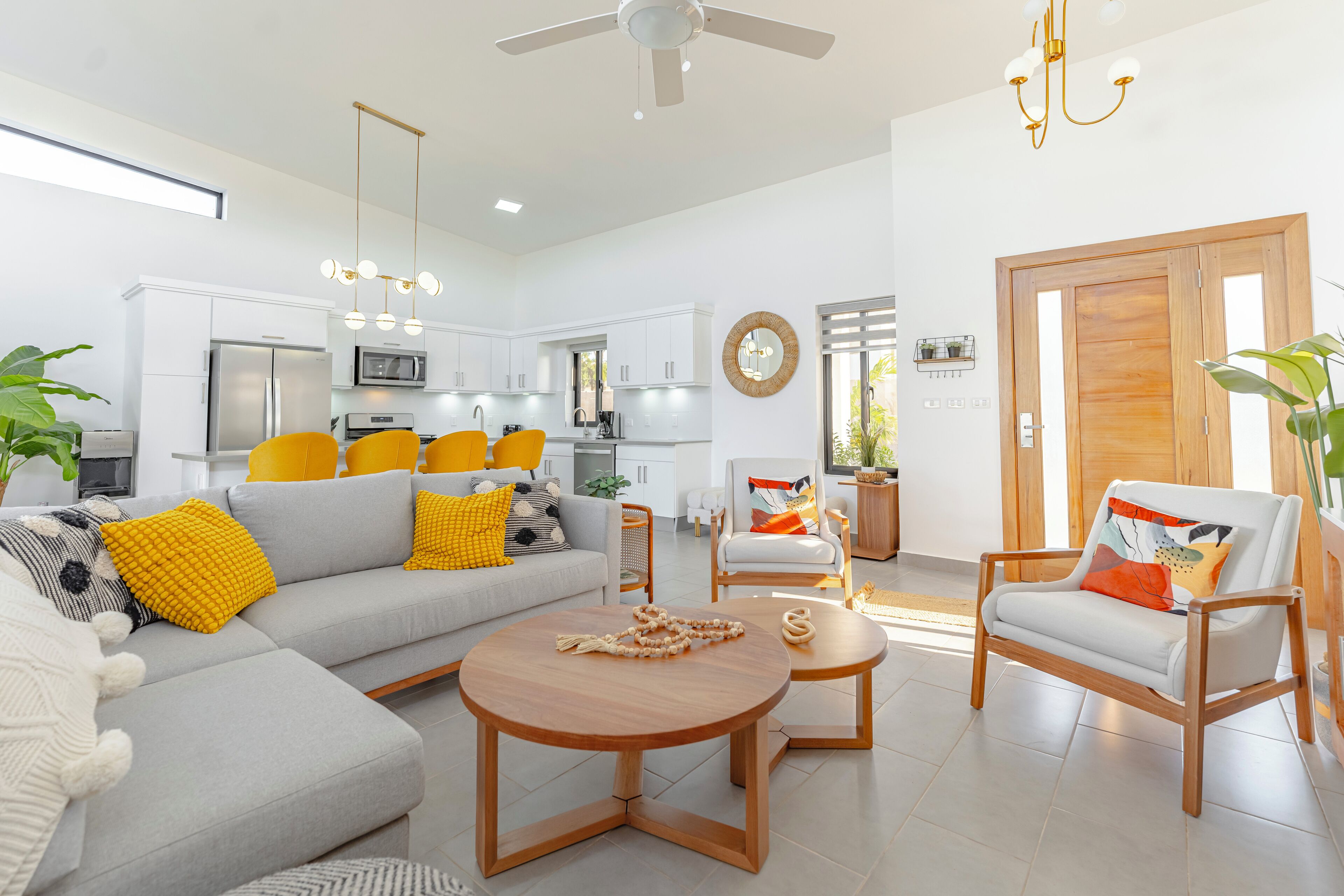 A modern living room with a grey sofa, yellow cushions, a wooden coffee table, and a white armchair with colorful cushions.