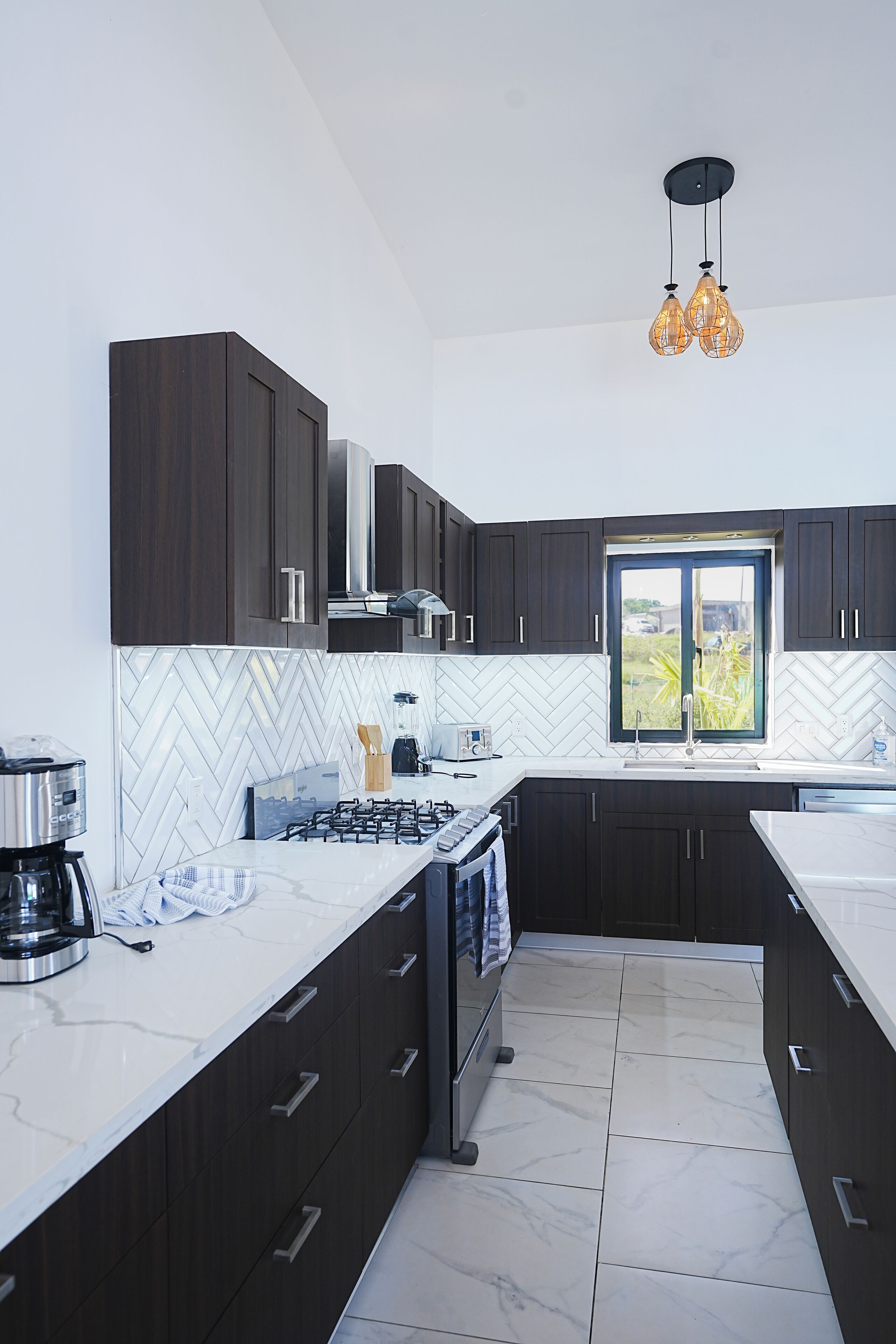 A modern kitchen with dark cabinets, a white herringbone backsplash, a gas stove, and a window with a view.