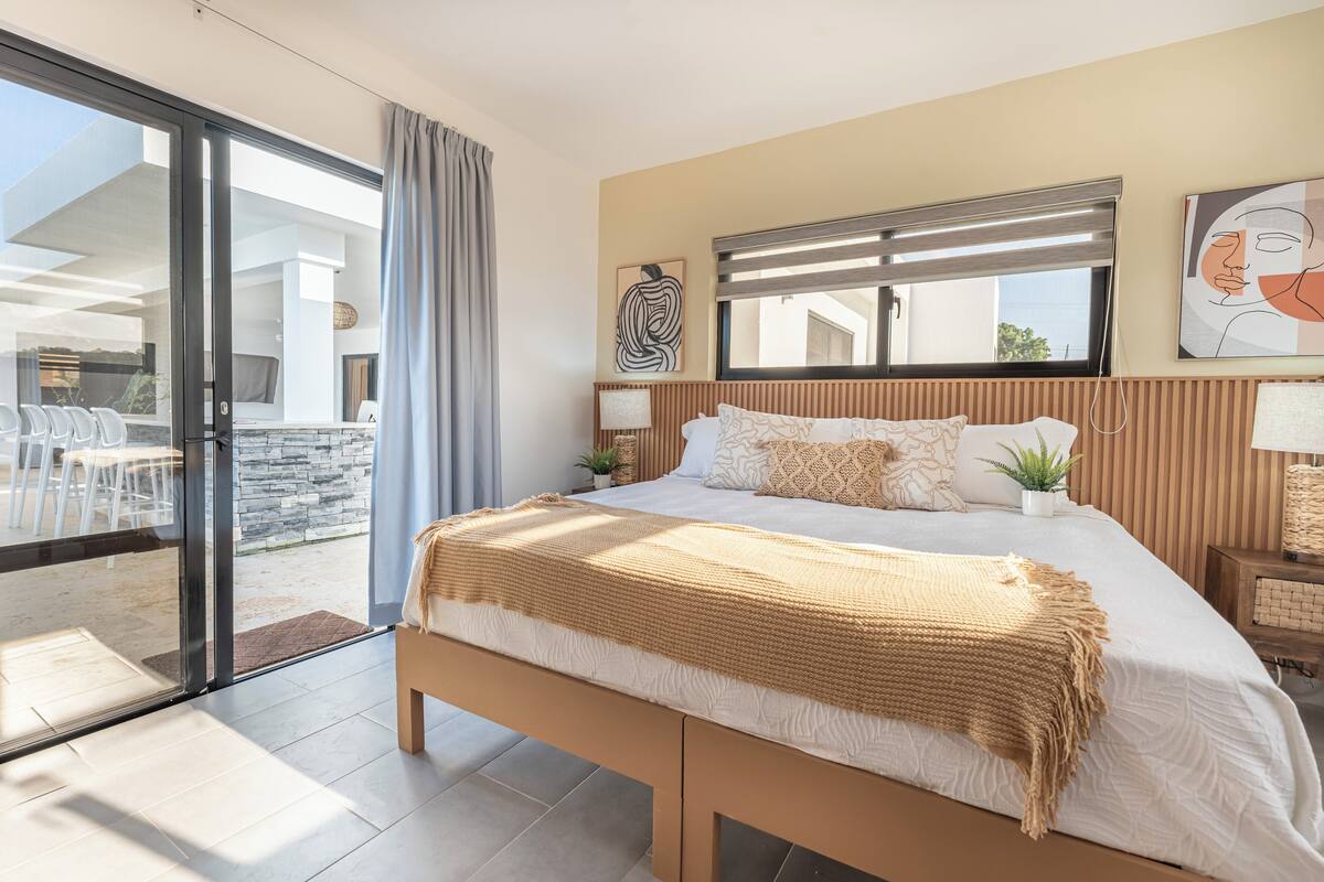 A modern bedroom with a large bed, a sliding glass door leading to an outdoor area, and a view of the outside.