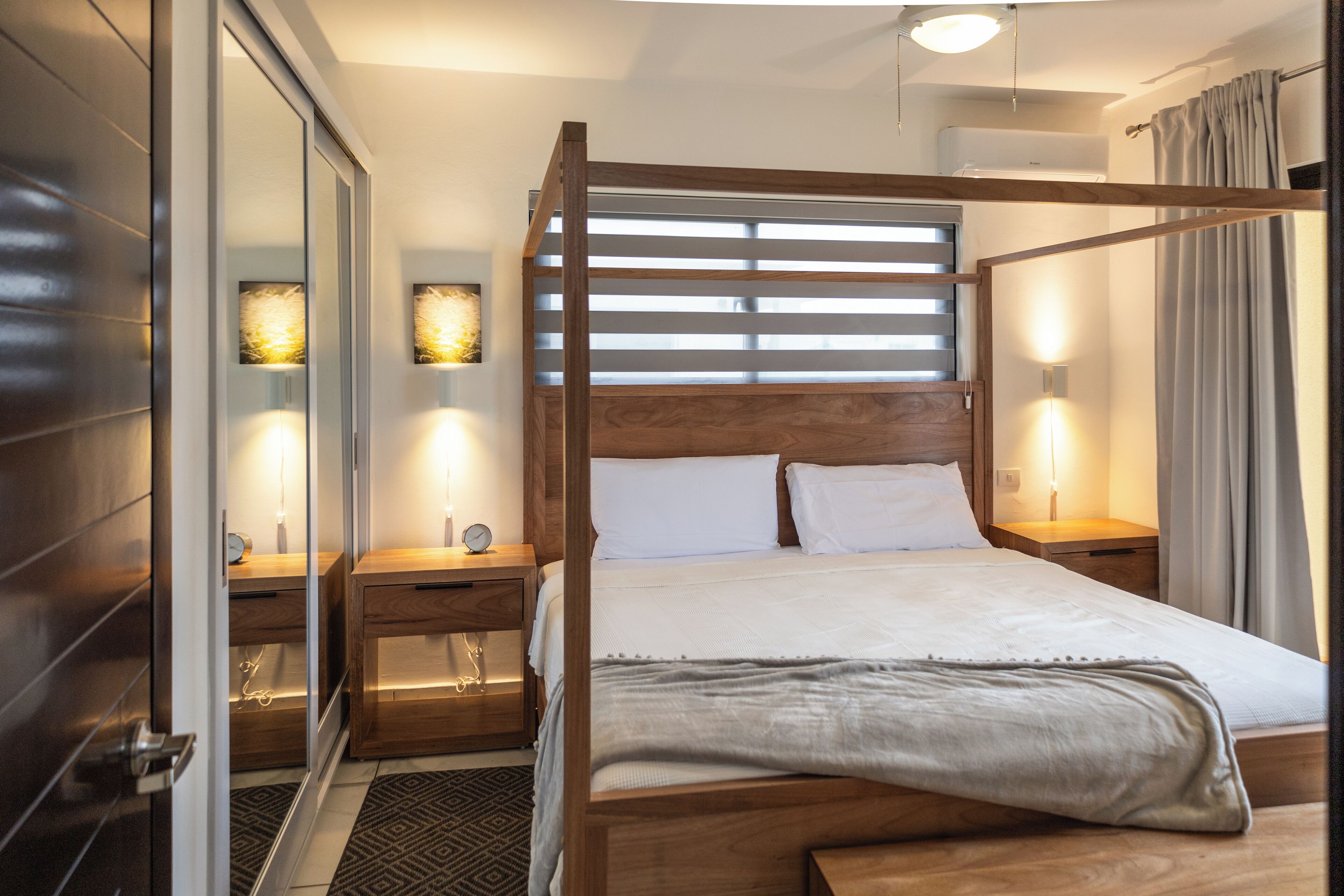 Una habitación de hotel moderna con una cama de madera, mesitas de noche y un espejo grande.