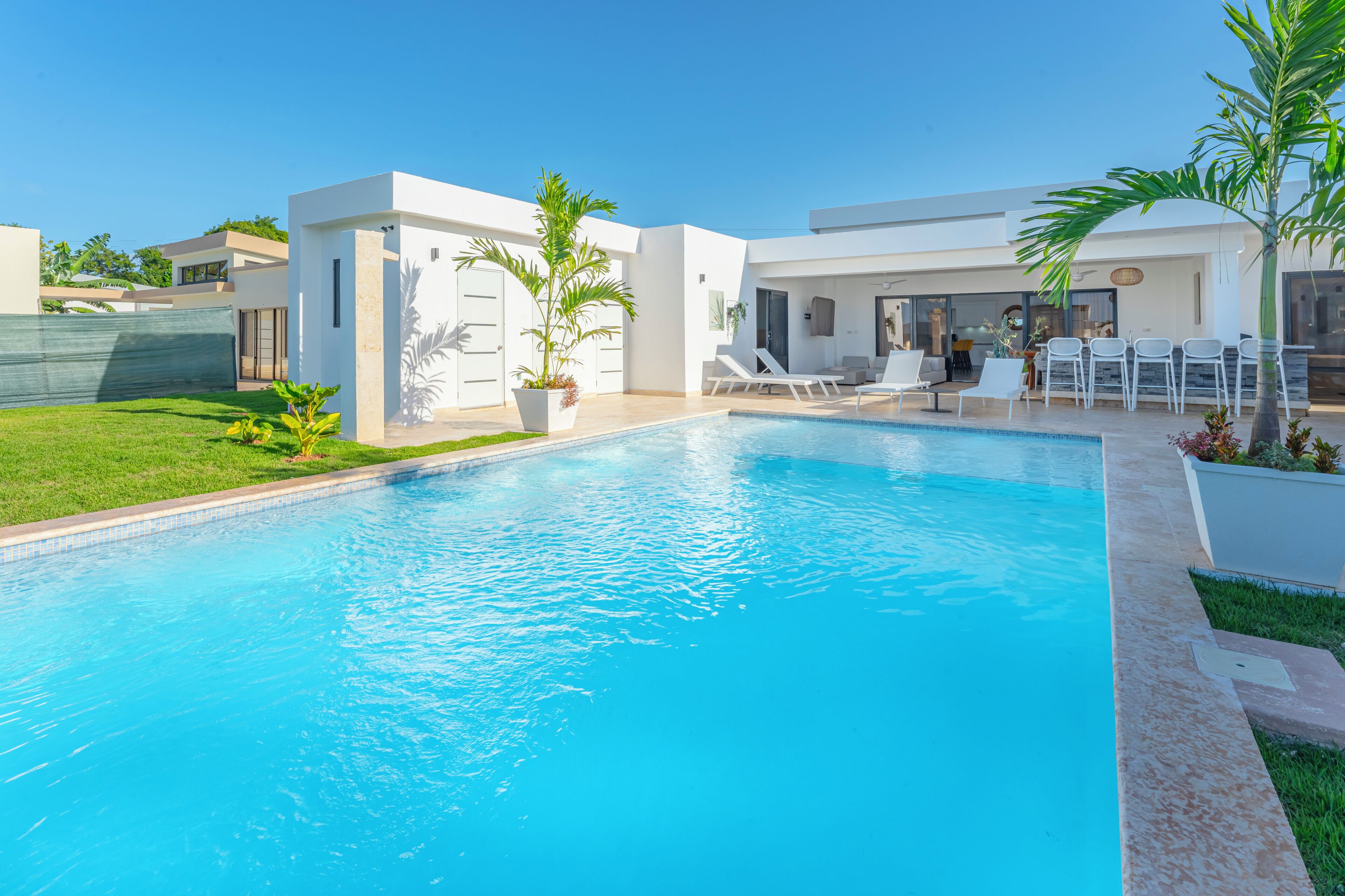A modern pool area with a clear blue pool, white lounge chairs, and a well-maintained lawn.