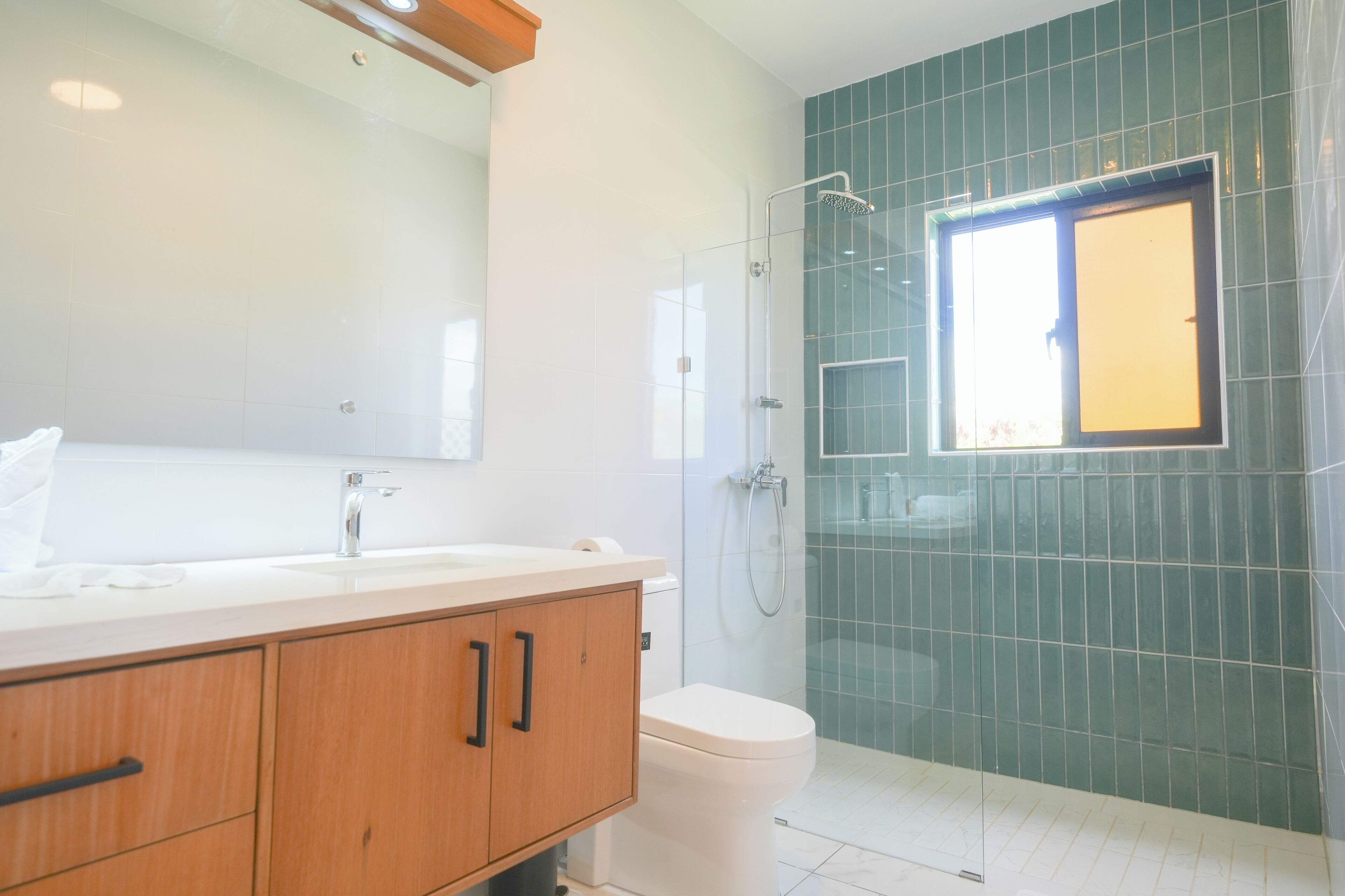 A modern bathroom with a white sink, wooden vanity, a glass shower enclosure, and green tiled walls.
