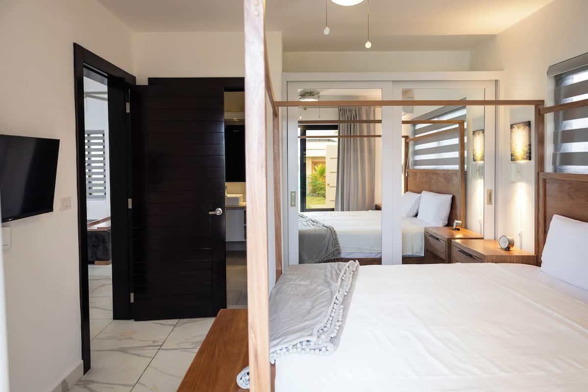 A hotel room with a large bed, a wooden headboard, a bedside table with a lamp, and a TV mounted on the wall.