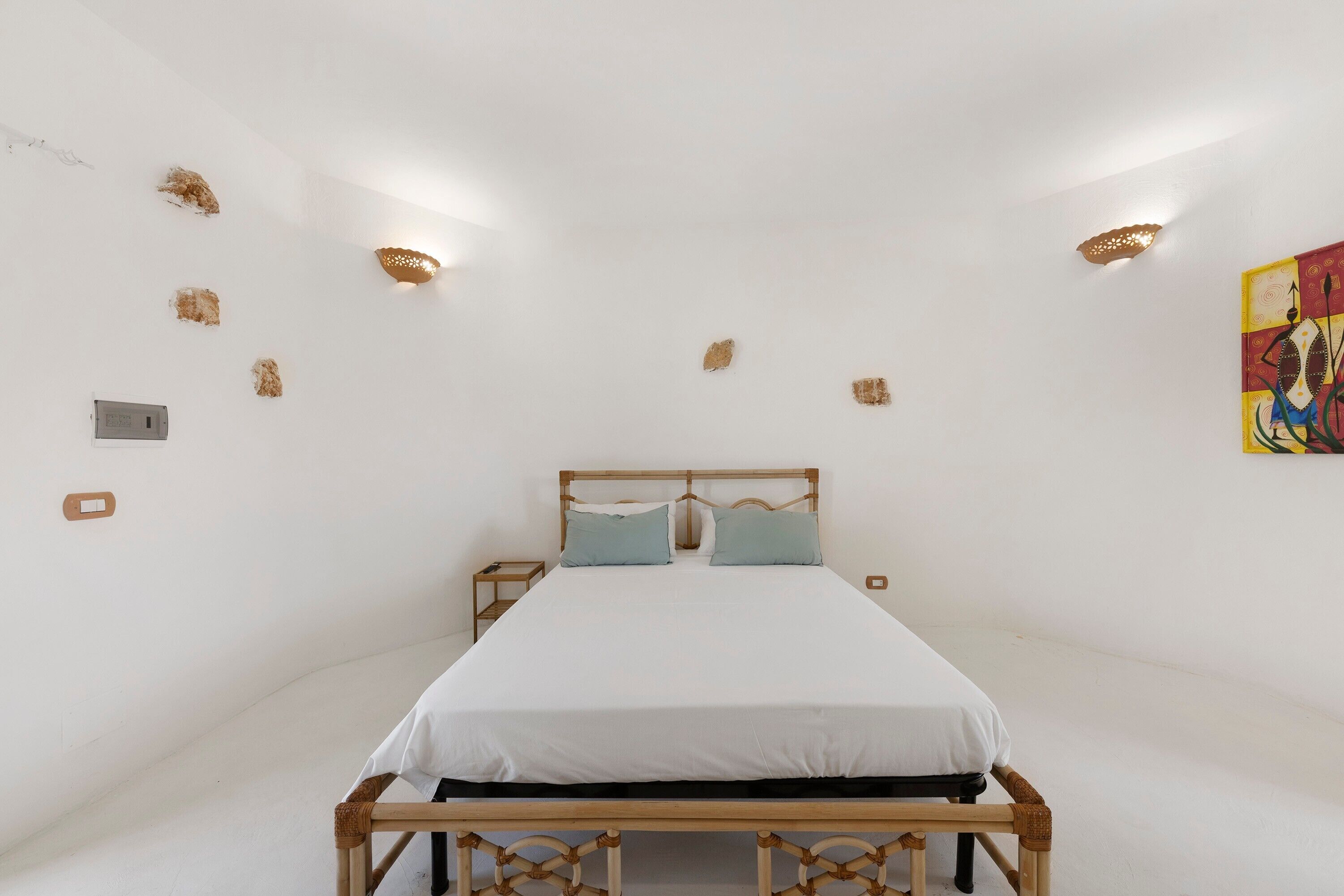 Un dormitorio con estructura de cama de madera, ropa de cama blanca y una mesita de noche pequeña.