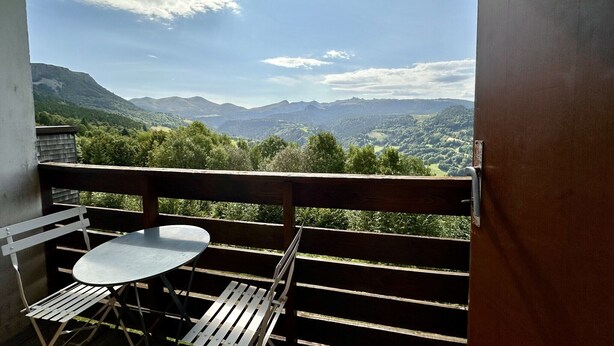 Un balcón con mesa y sillas, con vista a un paisaje montañoso.