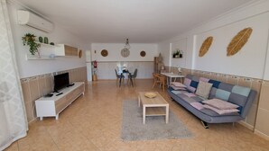 A living room with a TV, sofa, dining table, chairs, and a kitchen in the background. - Villa Mariamar with Private Pool, Wi-Fi, and Air Conditioning (Vale da Azinheira)