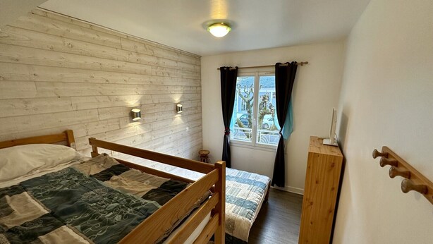 A small, cozy bedroom with a wooden bunk bed, a wooden wardrobe, and a window with curtains. - Sancy refuge by the snowy peak (Mont-Dore)
