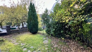 A garden with a stone pathway, a tall conifer, and dense foliage. - Sancy refuge by the snowy peak (Mont-Dore)