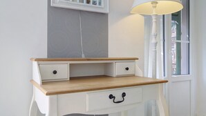 Een wit bureau met twee lades en een houten blad, geplaatst naast een raam met een witte lamp.