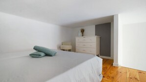 Een slaapkamer met een bed, een dressoir, een stoel en een vaas met gedroogde planten.