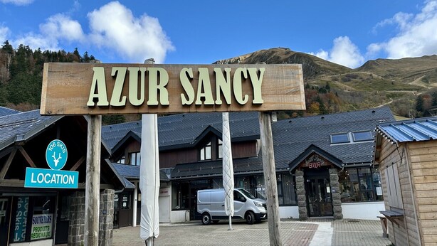 Ein Holzschild mit der Aufschrift 'AZUR SANCY' und einem Hinweisschild für '106 Skis'.