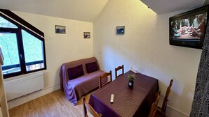 Ein gemütliches Zimmer mit Esstisch, einer Couch und einem an der Wand montierten Fernseher.