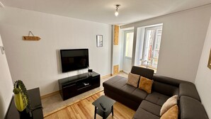 Ein modernes Wohnzimmer mit einem großen Flachbildfernseher, einem dunkelbraunen Sofa und einem kleinen schwarzen Couchtisch.