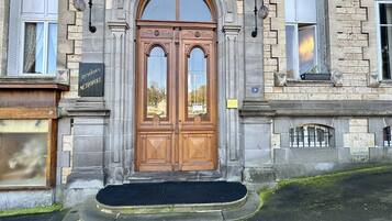 A stone building with a large wooden double door, a sign reading "Residence Métropole," and a small window with a barred view.