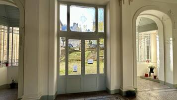 A grand entrance with a large arched doorway, a glass door with multiple panes, and a view of a garden and buildings outside.