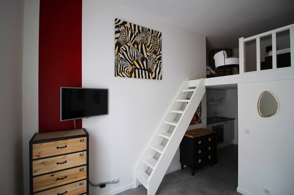 Une pièce avec un escalier blanc, un téléviseur à écran plat, une œuvre d’art aux motifs zébrés, un meuble en bois et un miroir rond.