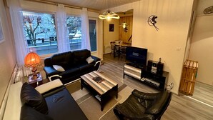 Un soggiorno con divano nero, tavolino, televisione e zona pranzo con tavolo e sedie.