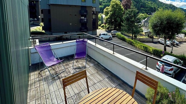 Un balcone con vista su una collina boscosa, un'area parcheggio e un edificio dal design moderno.