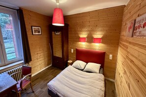 Une pièce aux murs lambrissés, contenant un lit, un bureau et une chaise.