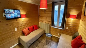 Una camera accogliente in stile chalet, con arredamento in legno, una televisione a parete e due letti con cuscini rossi e grigi.