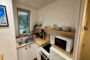 Une cuisine compacte avec des meubles blancs, un plan de travail en bois, un four à micro-ondes, une cuisinière et une fenêtre donnant sur un paysage verdoyant.
