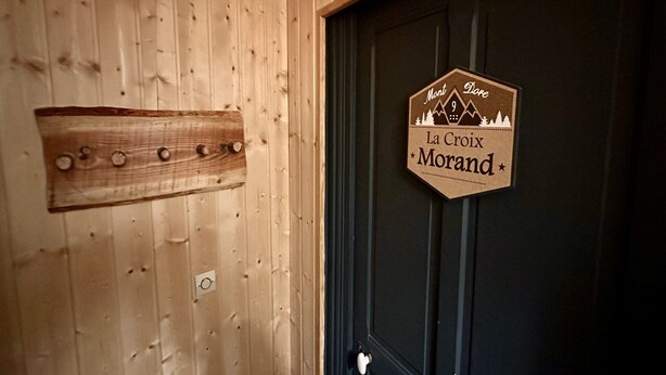 Un muro di legno con un cartello che riporta la scritta "Mon, Dore La Croix Morand" e un pannello di legno con fori circolari.