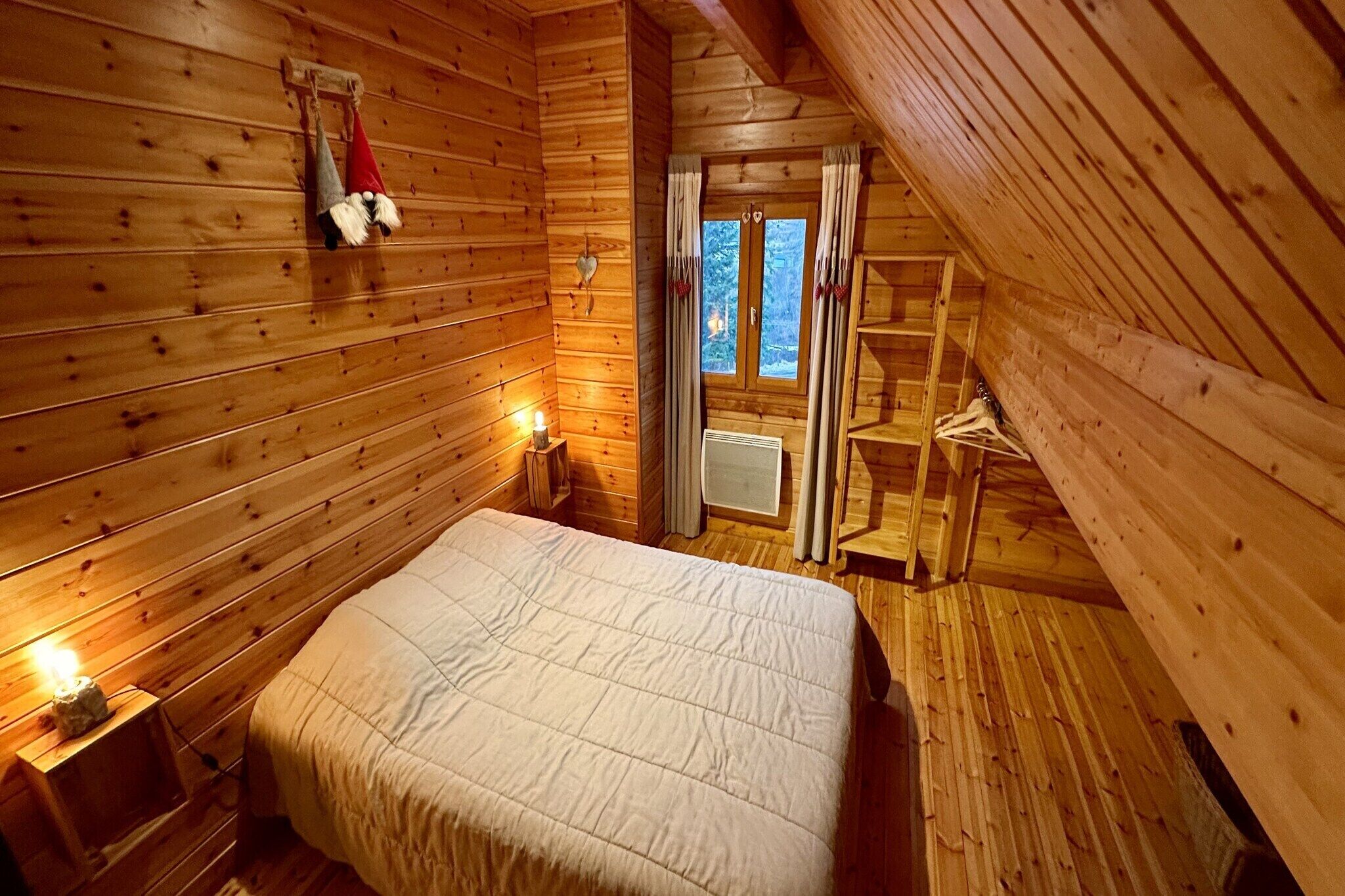 A cozy wooden cabin bedroom with a bed, a nightstand, a shelf, and a window with curtains.